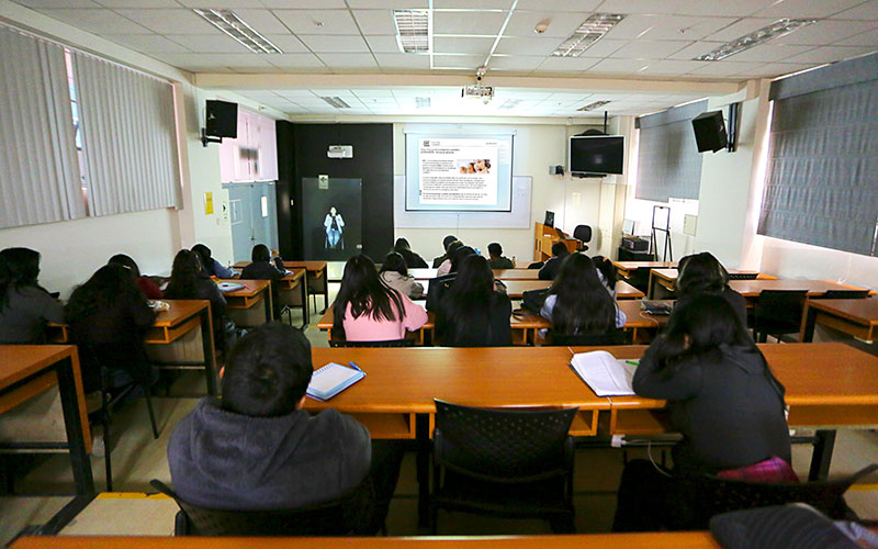 Aula moderna equipada con tecnología asistiva: pantallas táctiles, anillos de inducción para audífonos y mesas ajustables en altura